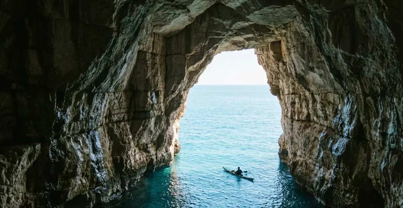 Vue en contre-plongée d'une grotte marine en Corse avec un kayakiste silhouetté contre l'entrée lumineuse