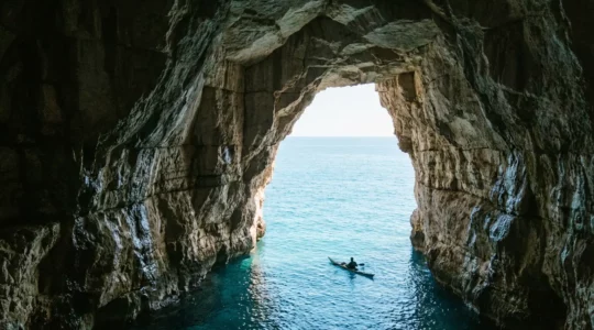 Vue en contre-plongée d'une grotte marine en Corse avec un kayakiste silhouetté contre l'entrée lumineuse