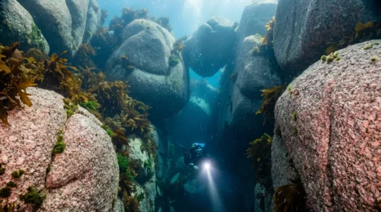 Plongeur explorant un labyrinthe de rochers granitiques sous-marins avec faisceau lumineux